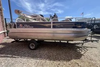 Slide: The Image of 2023 Sun Tracker Bass Buggy 18 DLX pontoon boat on a trailer under a clear blue sky. - 2