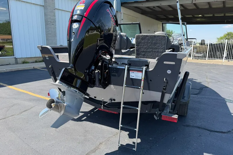 Slide: The Image of 2027 Lund 1875 Impact XS Sport boat with powerful outboard motor and ladder, parked outdoors. - 2