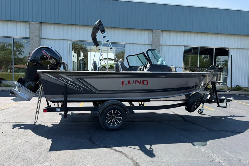 The Image of 2027 Lund 1875 Impact XS Sport boat on trailer, parked outside a building. - 0