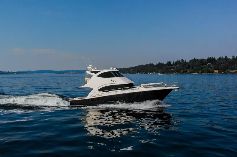 Slide: The Image of 2012 Riviera 33 Flybridge yacht cruising on a serene lake under a clear blue sky. - 39