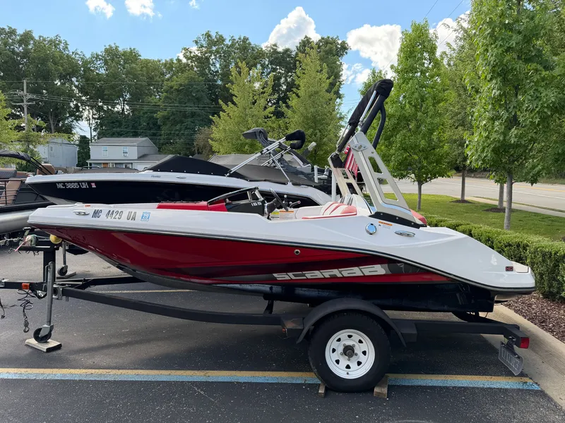 Slide: The Image of A 2017 Scarab 165 boat on a trailer, parked in a lot with trees in the background. - 2
