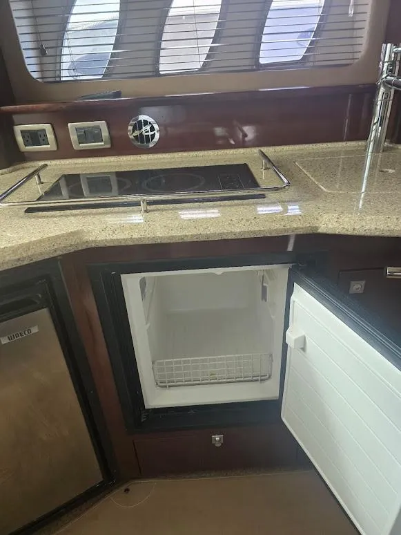 Slide: The Image of 2008 Sea Ray 40 Sundancer yacht kitchen with stove, sink, and open mini fridge. - 16