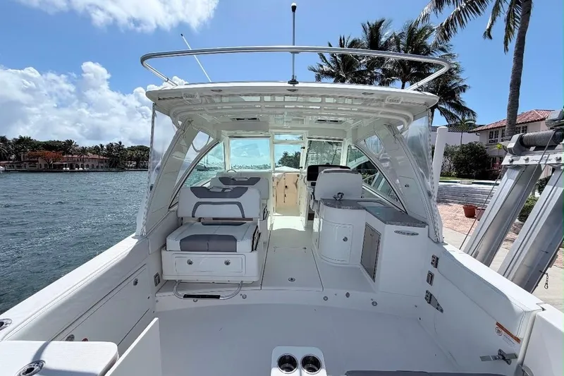 Slide: The Image of 2019 World Cat 320 DC boat interior with seating, docked by palm trees and waterfront homes. - 12