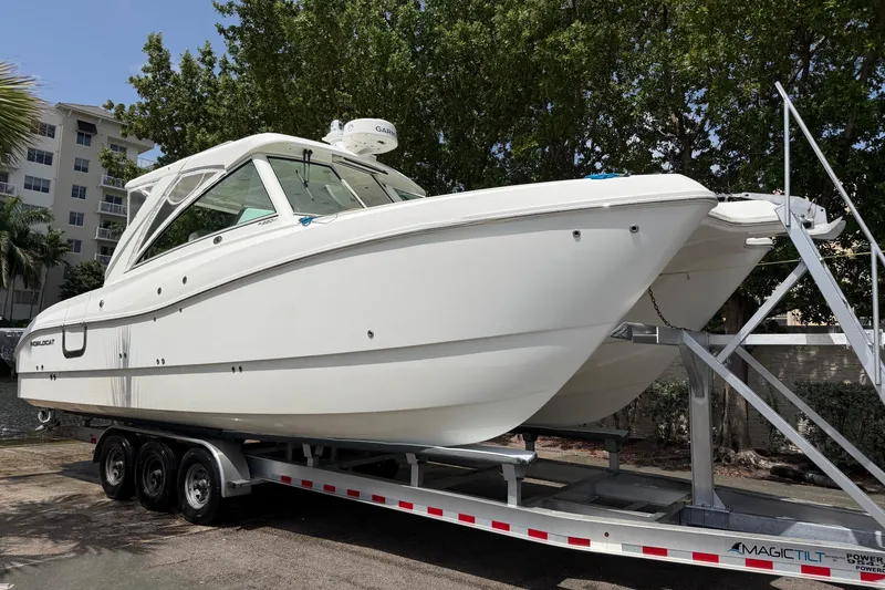 Slide: The Image of 2019 World Cat 320 DC boat on trailer, parked outdoors near trees and buildings. - 3