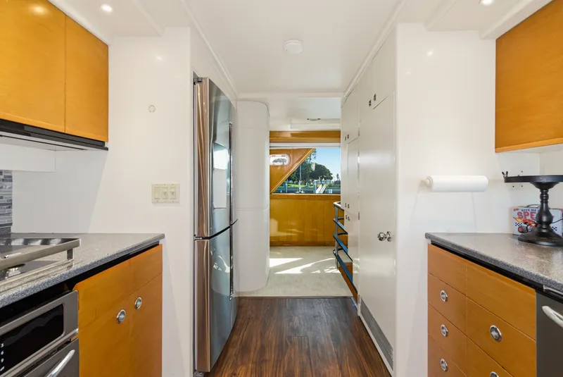 Slide: The Image of The yacht's kitchen features wooden cabinets, stainless steel appliances, and a view of the water. - 23
