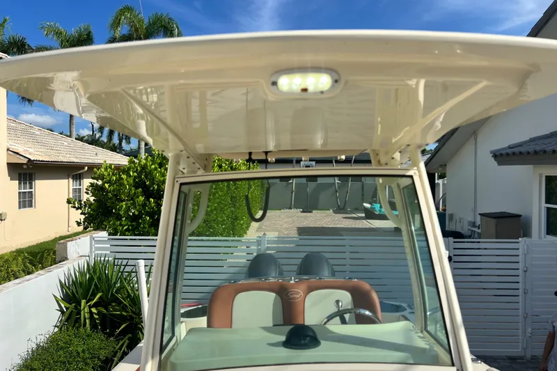 Slide: The Image of 2014 Scout 245 XSF boat with T-top and helm, parked in a residential driveway. - 86