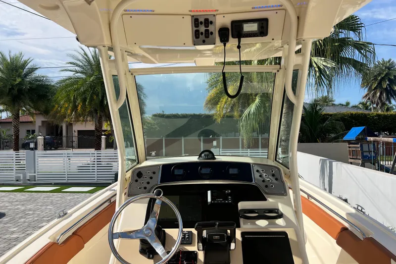 Slide: The Image of 2014 Scout 245 XSF boat cockpit with steering wheel and control panel, surrounded by palm trees. - 54