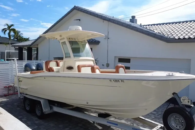 Slide: The Image of 2014 Scout 245 XSF boat on trailer, parked in driveway with palm trees and house in background. - 20
