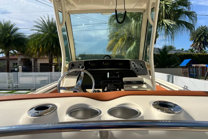 Slide: The Image of 2014 Scout 245 XSF boat dashboard with steering wheel, cup holders, and palm trees in the background. - 52