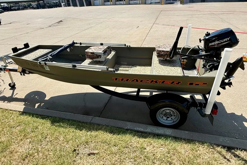 Slide: The Image of 2026 Tracker Grizzly 12 Jon boat with Mercury motor on trailer, parked outdoors. - 5