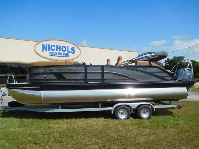 Slide: The Image of A 2026 Bennington 23 MSB pontoon boat on a trailer in front of a building with "Nichols Marine" sign. - 2