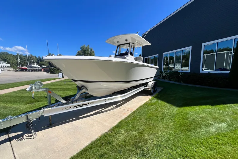 Slide: The Image of 2027 Pursuit S 268 Sport boat on trailer, parked on grass near a building. - 1