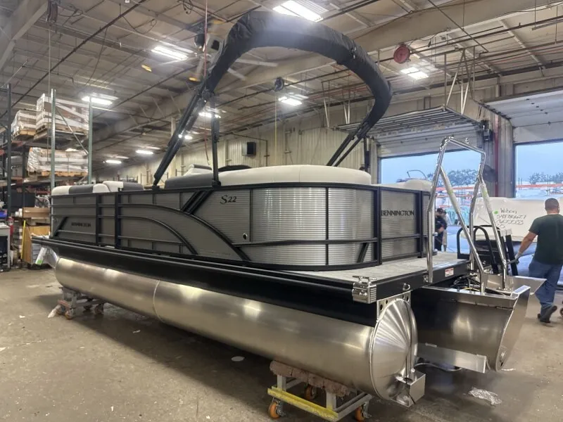 Slide: The Image of A Bennington 22 S1 pontoon boat is in a warehouse. It features a sleek design with a black Bimini top. - 3