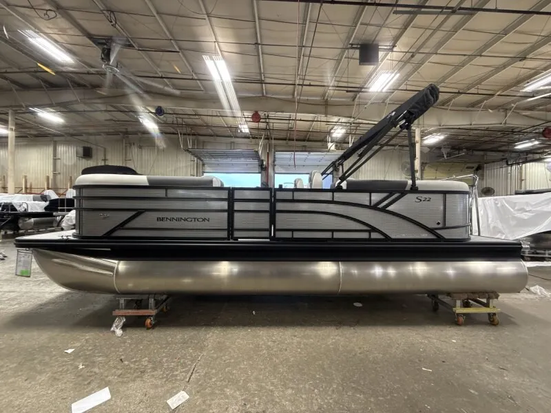 The Image of A Bennington 22 S1 Stern Radius pontoon boat is in a warehouse. It features a modern design with black railing. - 1