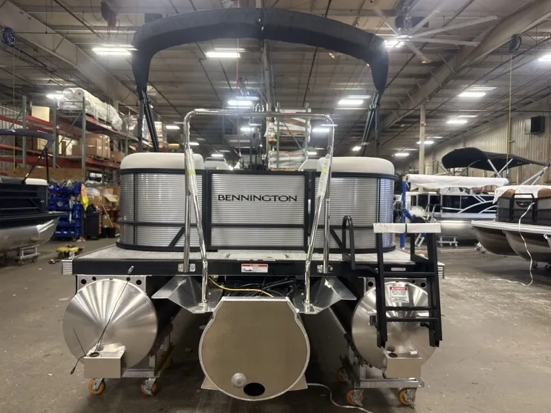 The Image of A Bennington 22 S1 Stern Radius pontoon boat in a warehouse. It features a black Bimini top. - 1