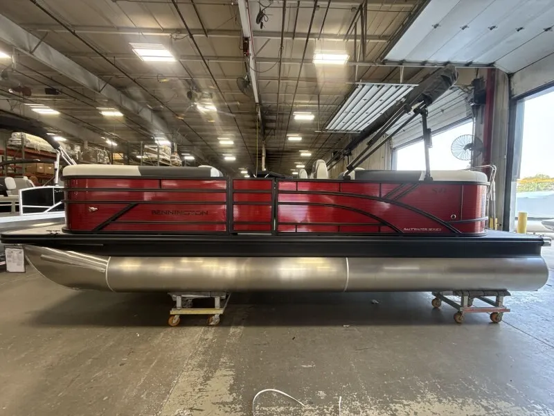 The Image of A 2027 Bennington 22 S1 Stern Radius pontoon boat is in a warehouse. It features red paneling and silver pontoons. - 1