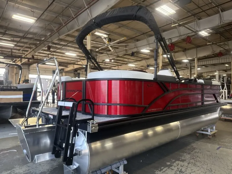 Slide: The Image of A red Bennington pontoon boat with a black Bimini top is in a warehouse. - 2