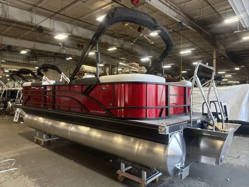 The Image of A red Bennington pontoon boat is in a warehouse. It features a black Bimini top. - 1