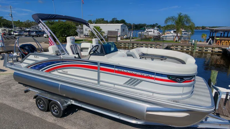 Slide: The Image of A 2027 Bennington 22 M Swingback pontoon boat on a trailer in a marina area. - 3