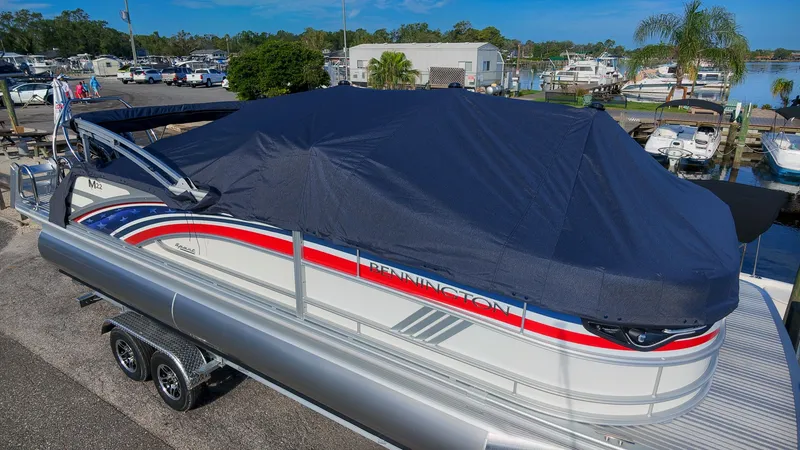 Slide: The Image of A 2027 Bennington 22 M Swingback pontoon boat with cover, on a trailer in a marina. - 2