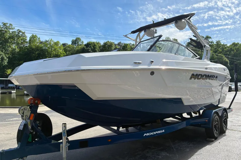 Slide: The Image of 2025 Moomba Max boat on trailer, sleek design, parked near water, sunny day. - 2