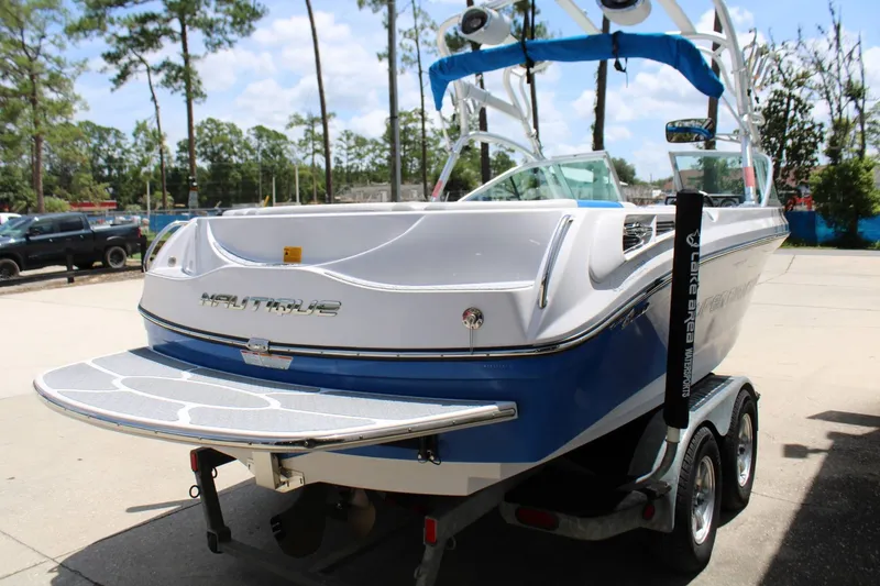 Slide: The Image of A 2008 Nautique 210 Team boat on a trailer, featuring a blue and white hull, parked outdoors. - 18