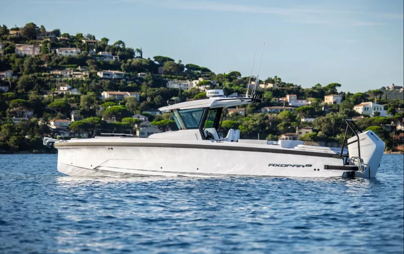 The Image of 2025 Axopar 29 CCX boat cruising on a scenic lake with hillside homes. - 10