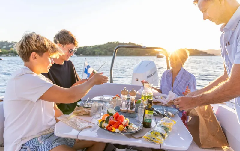 Slide: The Image of Family enjoying a meal on a 2025 Axopar 29 CCX boat at sunset. - 19