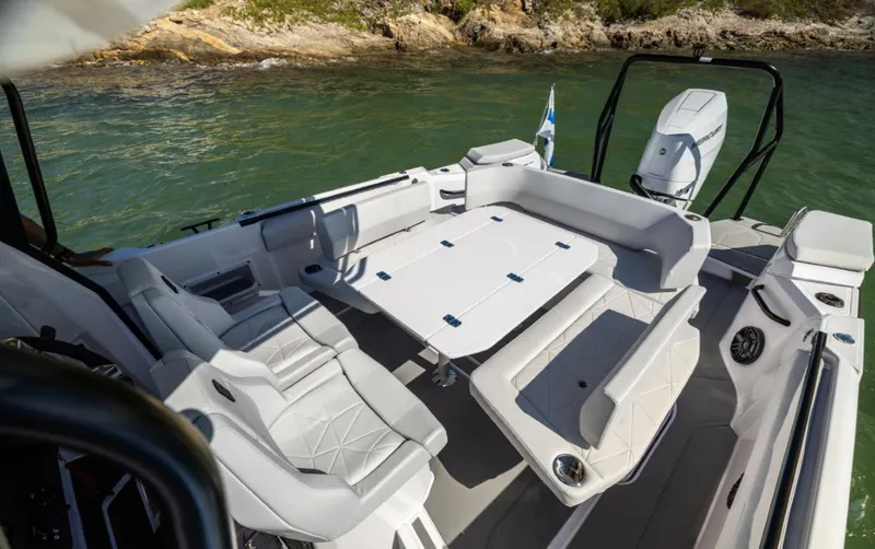 Slide: The Image of 2025 Axopar 29 CCX boat interior with seating and table, near rocky shoreline. - 17