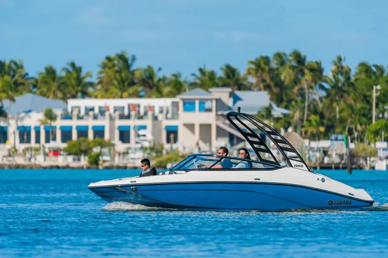 The Image of A 2024 Yamaha 195S boat cruising on calm water, surrounded by palm trees and buildings. - 8