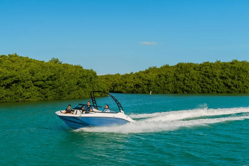 Slide: The Image of A 2024 Yamaha 195S boat speeds through turquoise water, surrounded by lush green trees. - 33