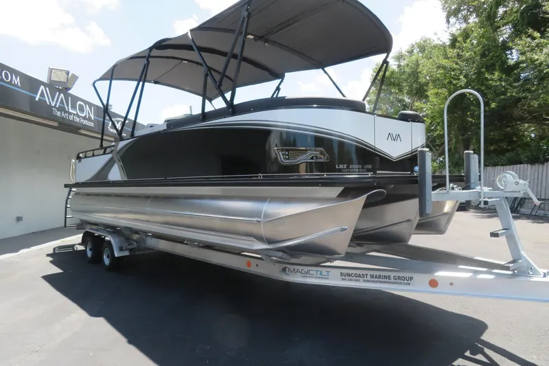 Slide: The Image of 2027 Avalon LSZ Versatile Rear Bench pontoon boat on trailer, parked outdoors. - 6