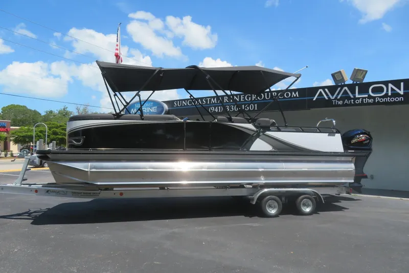 Slide: The Image of 2027 Avalon LSZ Versatile Rear Bench pontoon boat on trailer, parked outside dealership. - 0