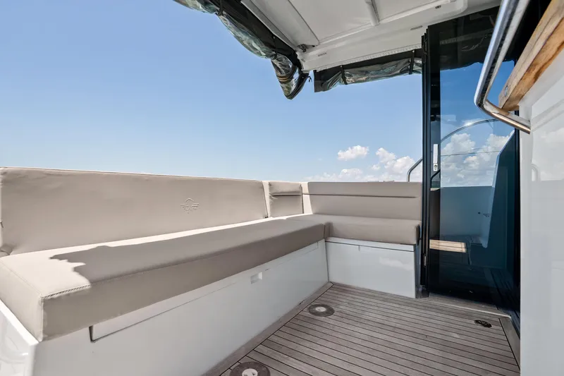 Slide: The Image of 2023 Sealine C335V yacht deck with cushioned seating and glass door under clear sky. - 11