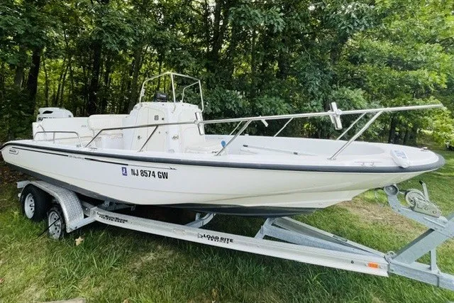 Slide: The Image of 2004 Boston Whaler 220 Dauntless boat on trailer, parked on grass near trees. - 2