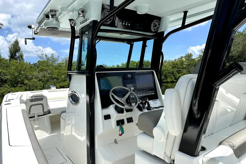 Slide: The Image of 2022 World Cat 325 CC boat interior with modern helm and seating, surrounded by lush greenery. - 9