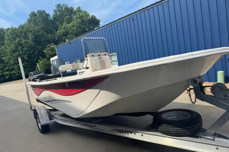 Slide: The Image of 2014 Carolina Skiff 198 DLV boat on trailer, parked near blue building. - 2