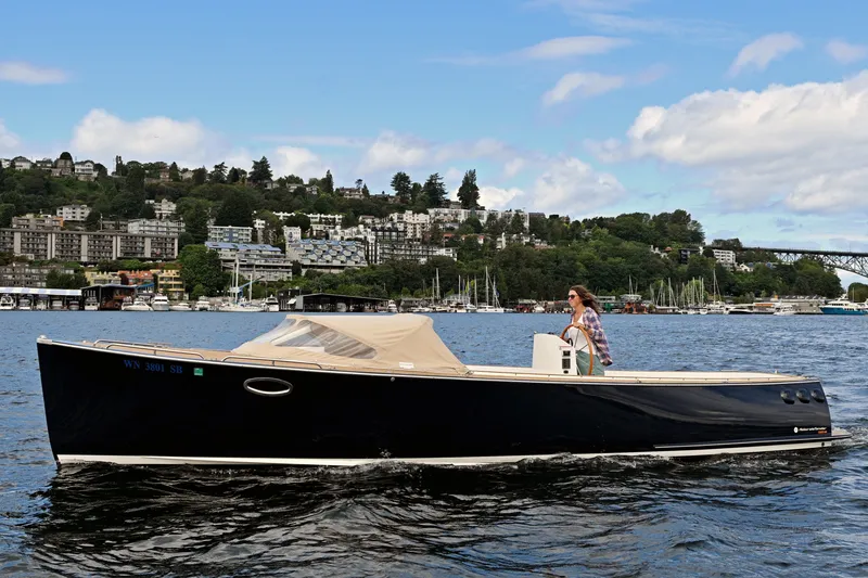The Image of 2013 AdmiralsTender C28 boat cruising on a scenic lake with a cityscape backdrop. - 0