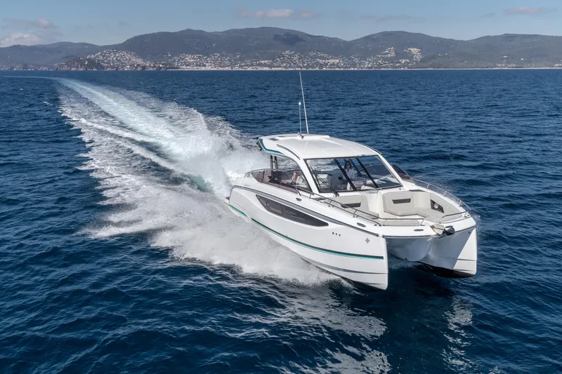 Slide: The Image of 2026 Jeanneau TH38 catamaran cruising on open sea with scenic mountain backdrop. - 10