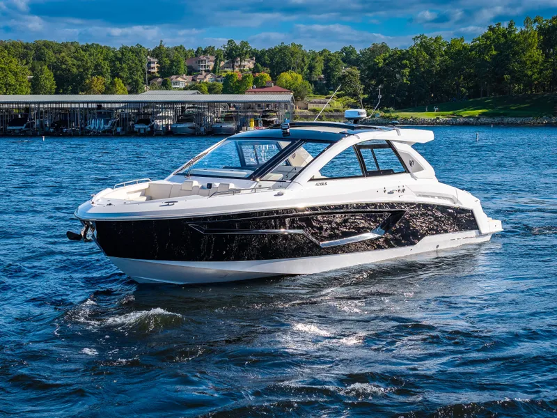 Slide: The Image of The 2027 Cruisers Yachts 42 GLS glides on a calm lake with a wooded shoreline in the background. - 6