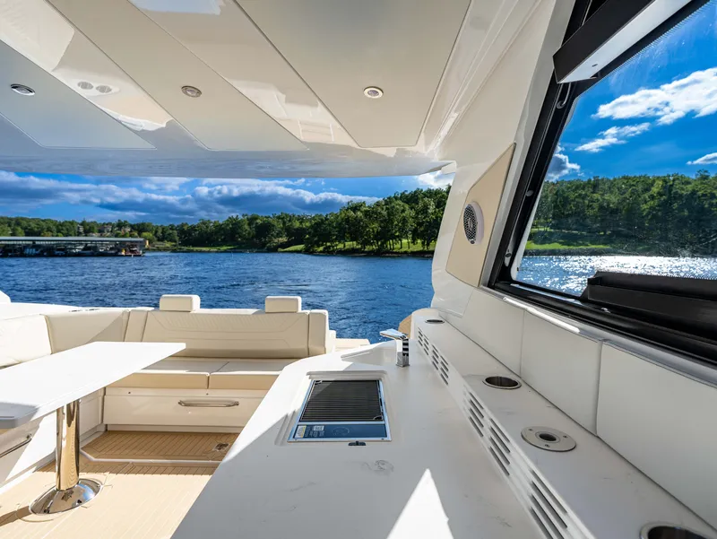 Slide: The Image of The image shows the deck of a 2027 Cruisers Yachts 42 GLS. It features elegant white seating and a table. A serene lake with wooded shores is visible in the background. - 30