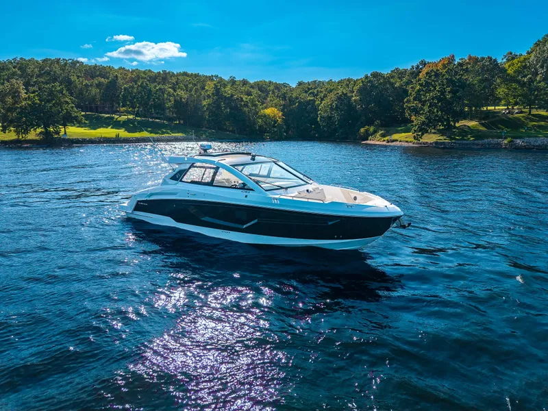 Slide: The Image of The 2027 Cruisers Yachts 42 GLS glides on a serene lake with wooded shores. - 23