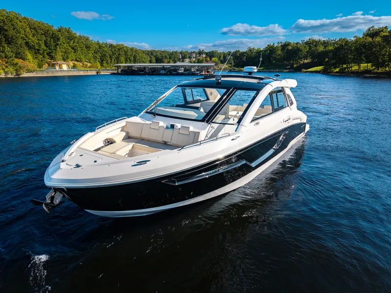 Slide: The Image of The 2027 Cruisers Yachts 42 GLS glides on a calm lake with a wooded shoreline. - 25
