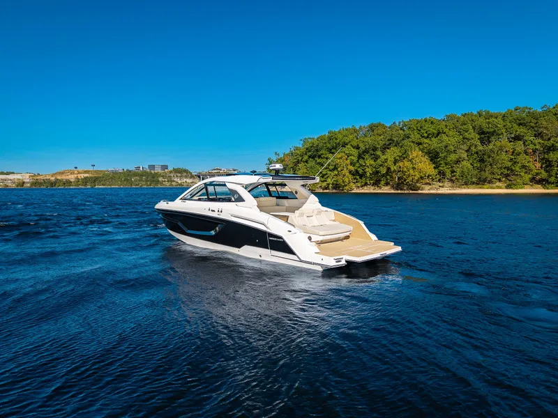 Slide: The Image of The 2027 Cruisers Yachts 42 GLS glides on calm waters with a wooded shoreline in the background. - 5