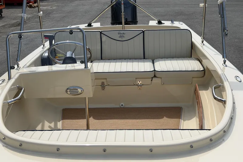 Slide: The Image of 2027 Rossiter 14 boat interior with white seating and steering wheel, docked on asphalt. - 19