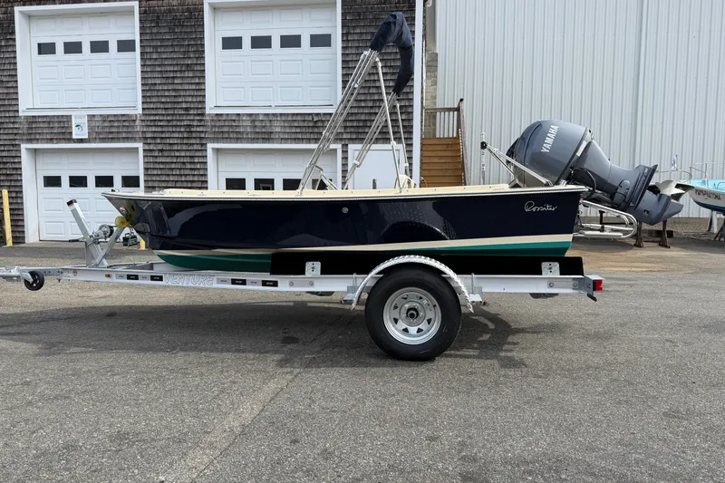 Slide: The Image of 2027 Rossiter 14 boat on trailer, parked outside a building with garage doors. - 6