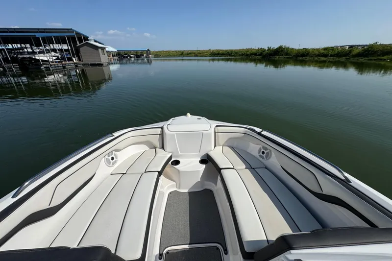 Slide: The Image of 2018 Yamaha Boats AR210 bow seating area on calm water near a marina. - 12