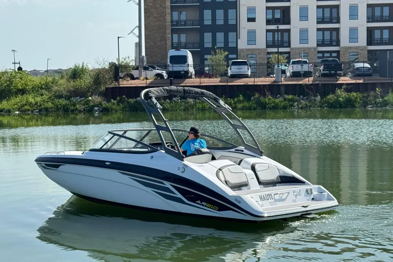 Slide: The Image of 2018 Yamaha AR210 boat cruising on a calm lake near modern buildings. - 1