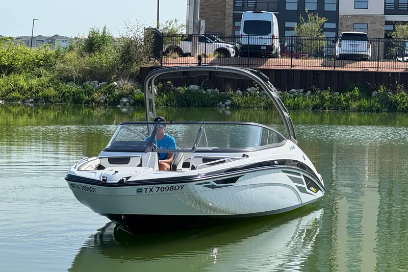 Slide: The Image of 2018 Yamaha Boats AR210 on calm water near a grassy shoreline. - 7