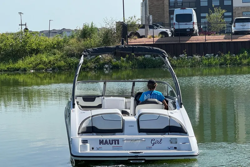 Slide: The Image of 2018 Yamaha Boats AR210 on a calm lake, surrounded by greenery and buildings. - 2